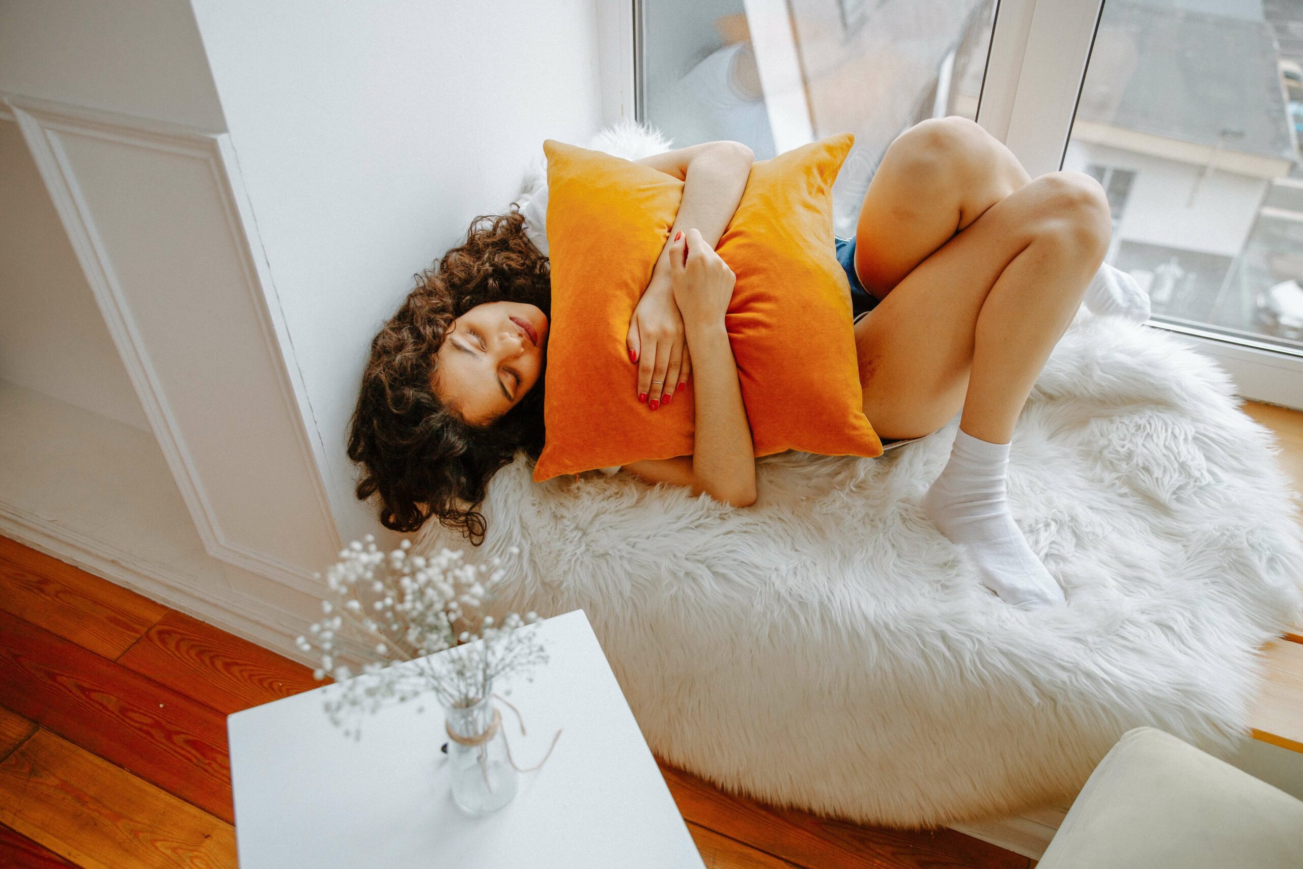 A woman snuggles with an orange pillow as she struggles with abdominal pain. Don't let IBS control your life, find relief in Pelvic Floor Physical Therapy in Washington, DC.