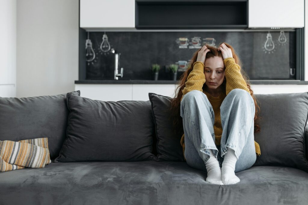 A woman sitting on the couch in despair. This could symbolize chronic perlvic pain that pelvic pain therapy in Washington, DC can help you address. Search for chronic pelvic pain in Washington, DC for help today.
